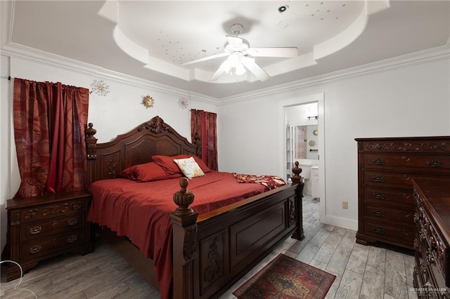 bedroom featuring ceiling fan, light wood-type flooring, ornamental molding, connected bathroom, and a tray ceiling