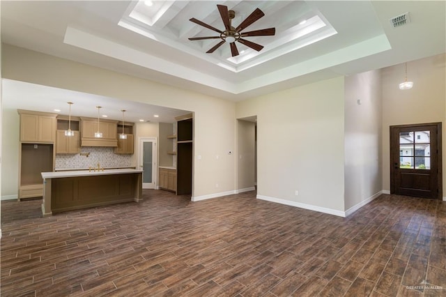 unfurnished living room featuring ceiling fan, a tray ceiling, dark hardwood / wood-style flooring, and a high ceiling