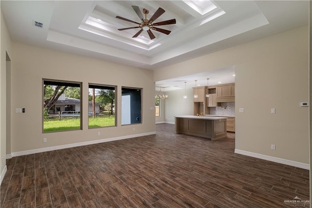 unfurnished living room with dark hardwood / wood-style floors, a skylight, a raised ceiling, and ceiling fan with notable chandelier