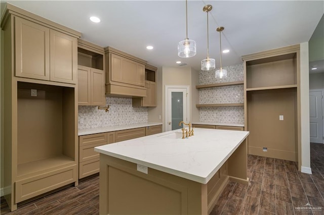 kitchen featuring sink, light stone counters, an island with sink, decorative backsplash, and decorative light fixtures