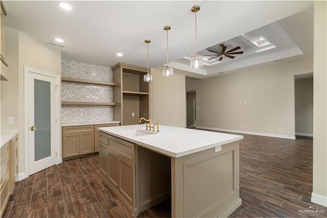 kitchen with sink, ceiling fan, a kitchen island with sink, hanging light fixtures, and a tray ceiling