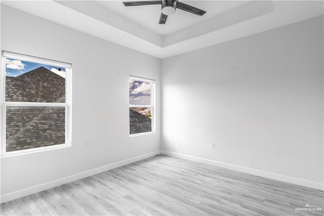 empty room with ceiling fan, light wood-type flooring, and a tray ceiling