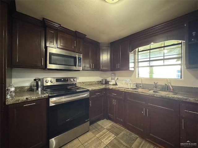kitchen featuring dark brown cabinets, dark stone counters, a sink, light tile patterned floors, and stainless steel appliances