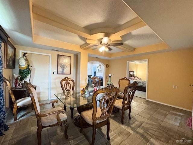 dining space with a ceiling fan, arched walkways, baseboards, and a raised ceiling