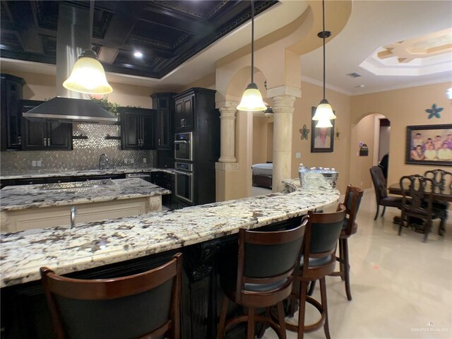 kitchen with decorative backsplash, a tray ceiling, crown molding, light stone counters, and arched walkways