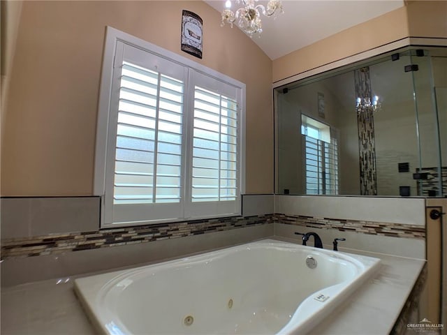 full bath featuring a whirlpool tub, a notable chandelier, and vaulted ceiling