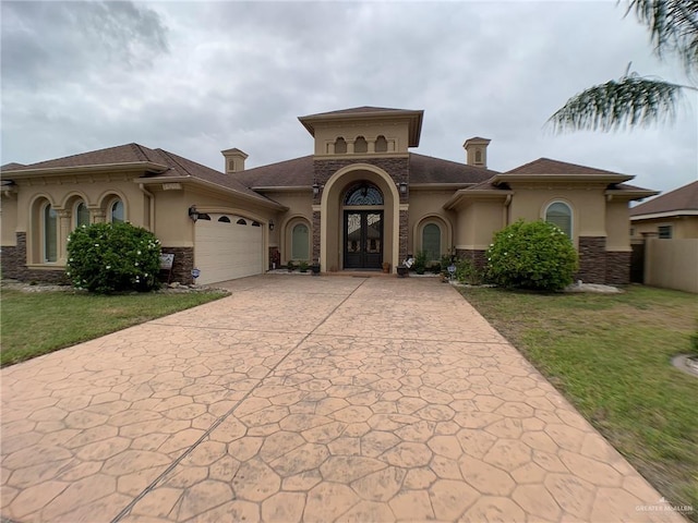 mediterranean / spanish home featuring stucco siding, a garage, stone siding, a front yard, and concrete driveway