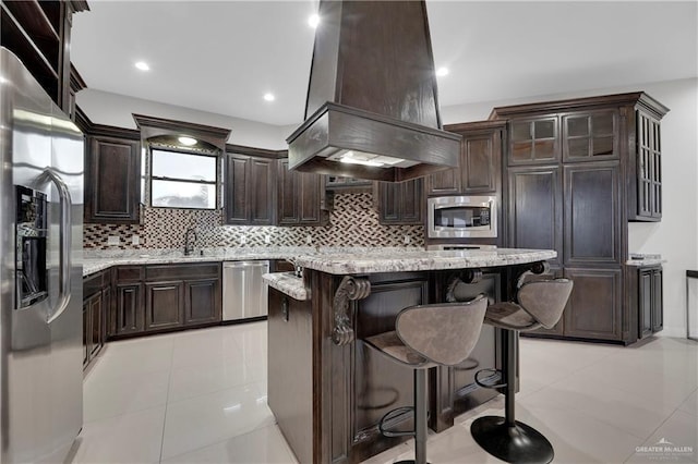 kitchen with island exhaust hood, appliances with stainless steel finishes, light tile patterned floors, and a kitchen breakfast bar