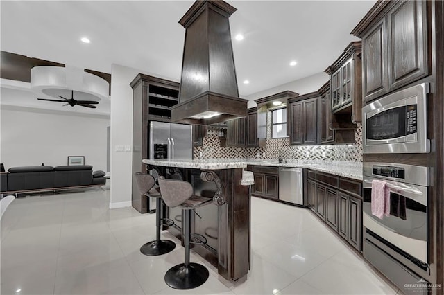 kitchen with dark brown cabinets, stainless steel appliances, a center island, tasteful backsplash, and island exhaust hood