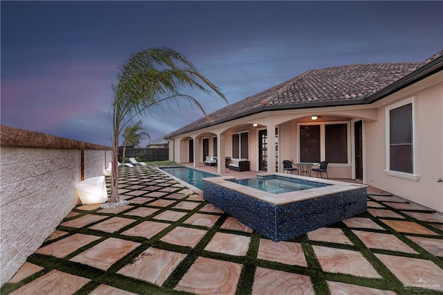 pool at dusk with a patio and an in ground hot tub