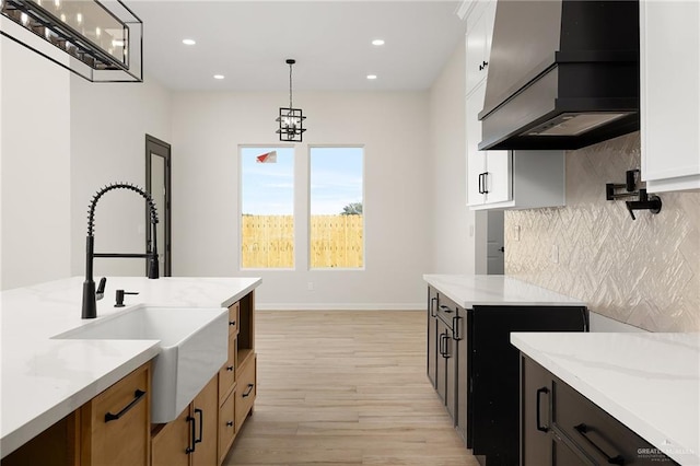 kitchen with custom exhaust hood, sink, hanging light fixtures, light stone counters, and white cabinetry