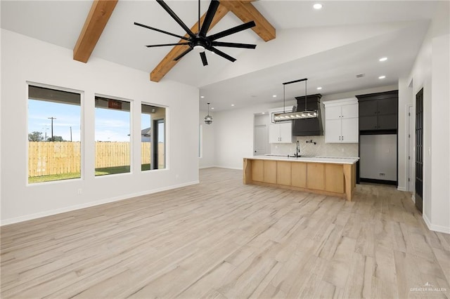 kitchen featuring decorative backsplash, lofted ceiling with beams, decorative light fixtures, light hardwood / wood-style floors, and an island with sink