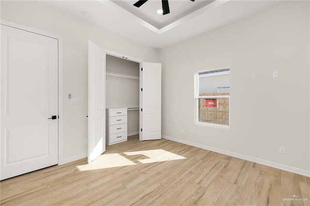 unfurnished bedroom featuring a raised ceiling, ceiling fan, and light hardwood / wood-style floors