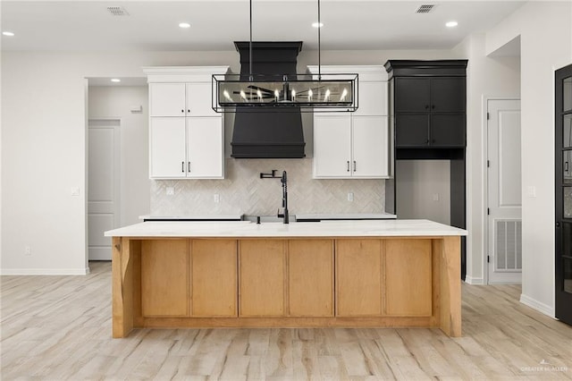 kitchen with a center island with sink, white cabinets, and light hardwood / wood-style floors