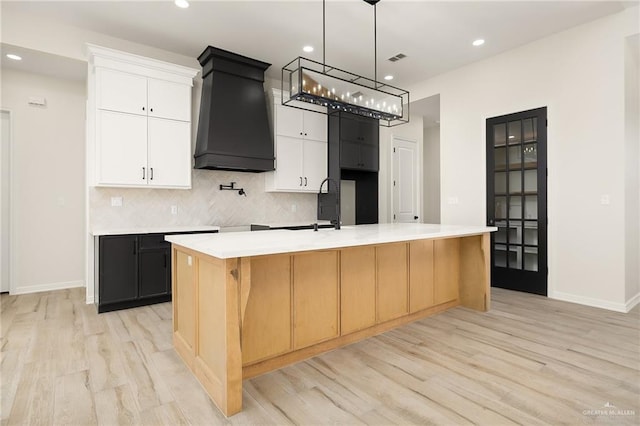 kitchen with custom exhaust hood, decorative backsplash, light wood-type flooring, a large island, and white cabinetry