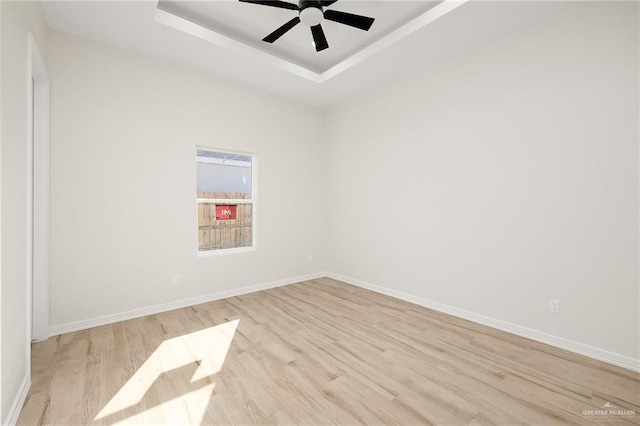 spare room with ceiling fan, light hardwood / wood-style floors, and a raised ceiling