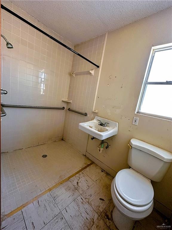 bathroom with tiled shower, toilet, sink, and a textured ceiling