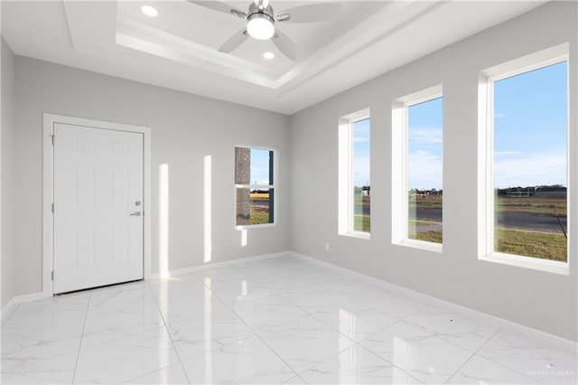 spare room featuring ceiling fan, a healthy amount of sunlight, and a tray ceiling