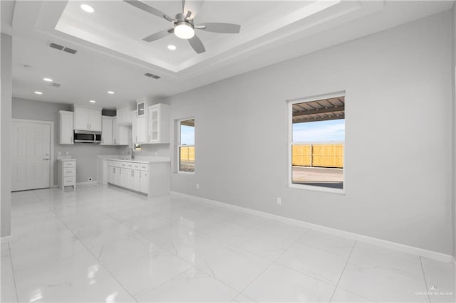 unfurnished living room with a tray ceiling, ceiling fan, a healthy amount of sunlight, and sink