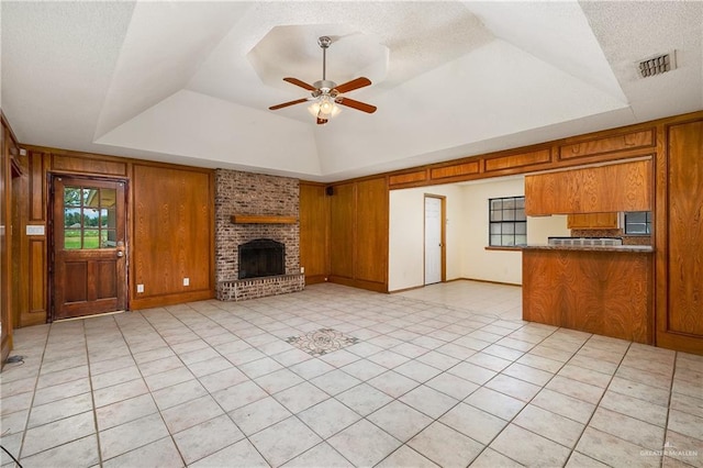 unfurnished living room featuring a tray ceiling, wood walls, a fireplace, and ceiling fan