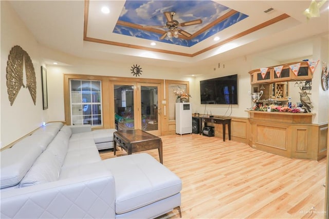 living room with light wood-type flooring, a tray ceiling, and ceiling fan