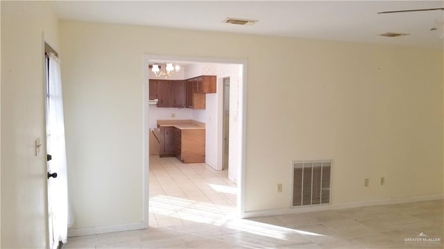 empty room with a notable chandelier and light tile patterned floors