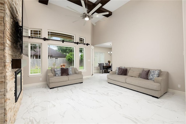 living room featuring marble finish floor, baseboards, high vaulted ceiling, a stone fireplace, and ceiling fan with notable chandelier