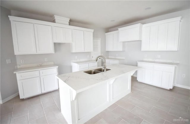 kitchen featuring light stone counters, sink, white cabinetry, and an island with sink