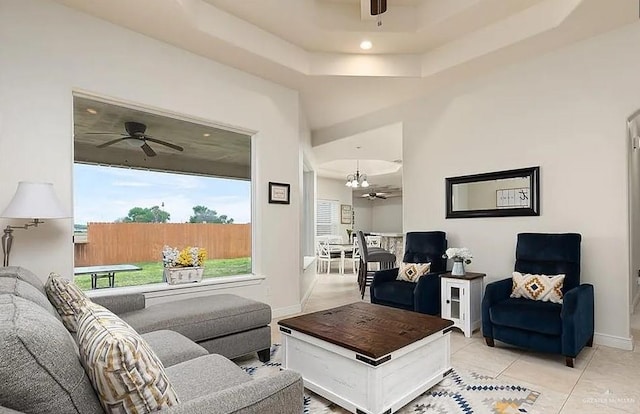 living area with a raised ceiling, baseboards, light tile patterned floors, and ceiling fan with notable chandelier