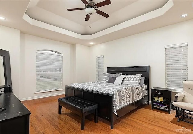 bedroom featuring a raised ceiling, baseboards, recessed lighting, and wood finished floors