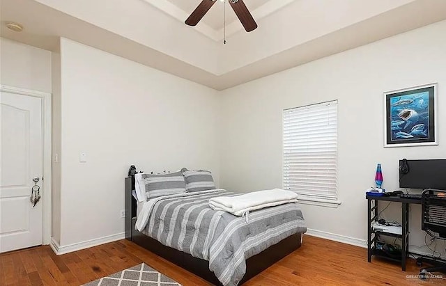bedroom featuring baseboards, ceiling fan, wood finished floors, and a tray ceiling