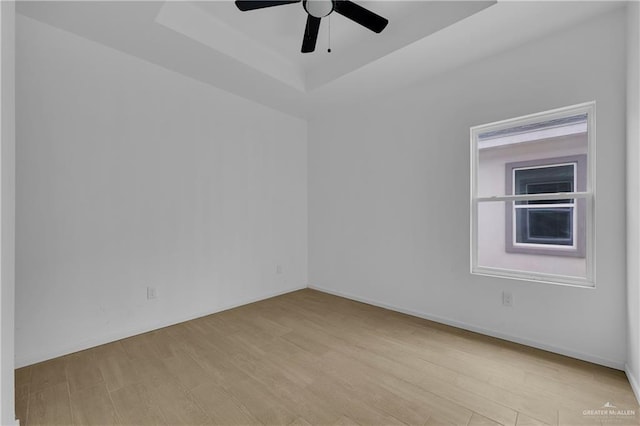 unfurnished room featuring ceiling fan, light wood-style flooring, baseboards, and a raised ceiling