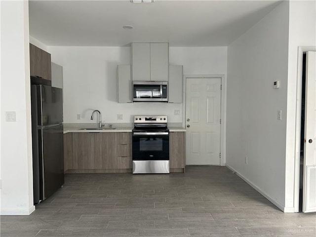 kitchen with a sink, light countertops, appliances with stainless steel finishes, wood tiled floor, and modern cabinets