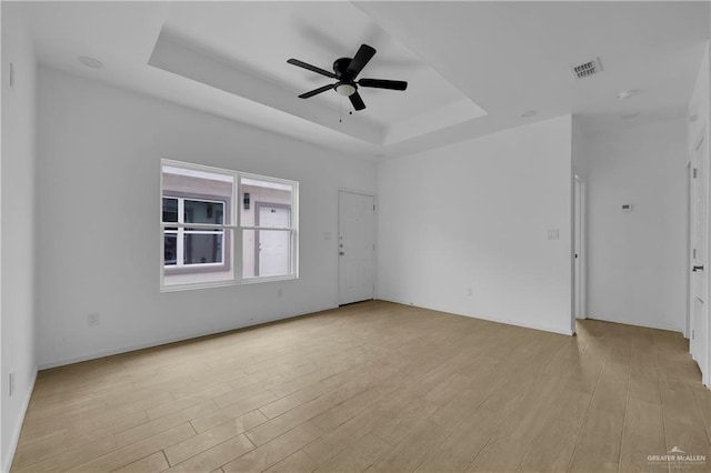 spare room featuring light wood-style floors, visible vents, a tray ceiling, and a ceiling fan