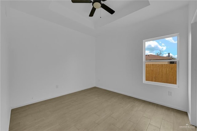 spare room with light wood-style floors, baseboards, a raised ceiling, and a ceiling fan