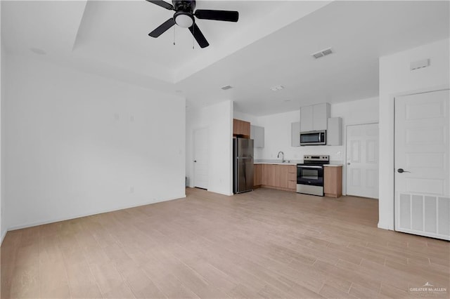 unfurnished living room with light wood-style flooring, visible vents, ceiling fan, and a tray ceiling