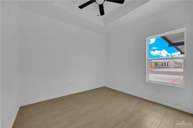 unfurnished room with light wood finished floors, baseboards, and a tray ceiling