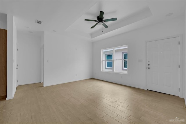 interior space with a raised ceiling, visible vents, light wood-style flooring, ceiling fan, and baseboards