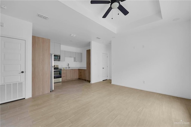 unfurnished living room with a tray ceiling, a sink, visible vents, and light wood-style floors