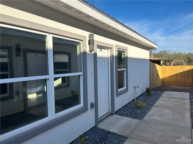 view of exterior entry featuring a patio area, fence, and stucco siding