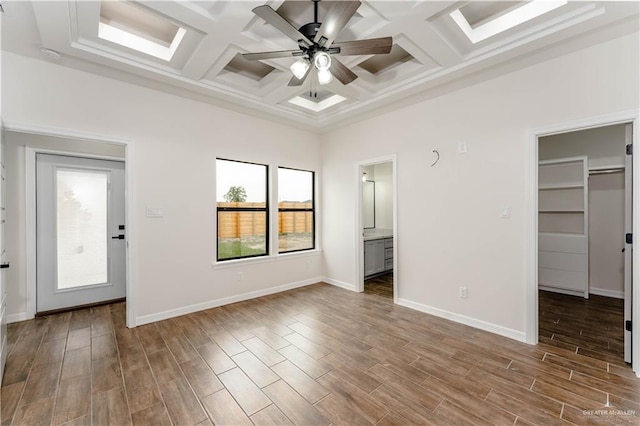 unfurnished bedroom featuring coffered ceiling, ceiling fan, a spacious closet, beam ceiling, and wood-type flooring