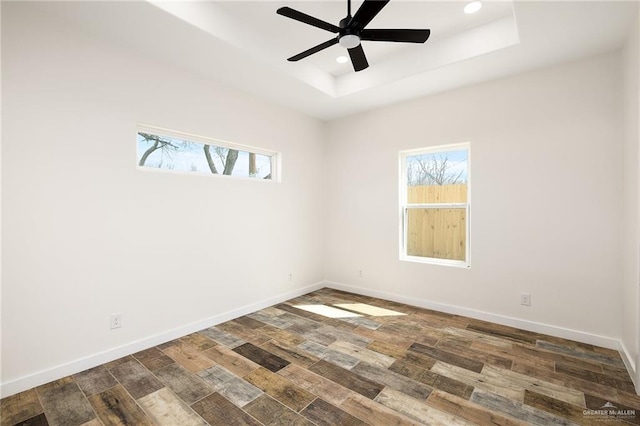 spare room with a raised ceiling, ceiling fan, a healthy amount of sunlight, and dark hardwood / wood-style flooring