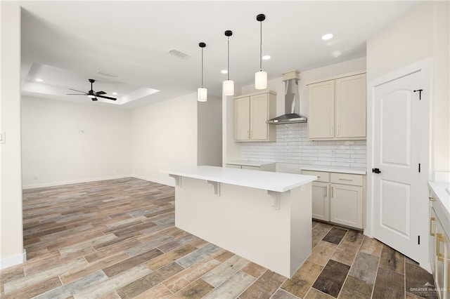 kitchen with wall chimney exhaust hood, tasteful backsplash, a center island, hanging light fixtures, and a tray ceiling