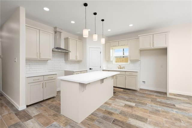 kitchen featuring a breakfast bar, hanging light fixtures, a kitchen island, wall chimney range hood, and backsplash