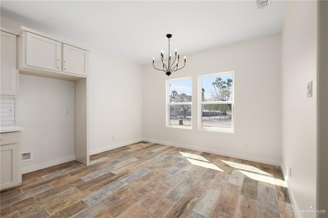 unfurnished dining area featuring an inviting chandelier and light hardwood / wood-style flooring