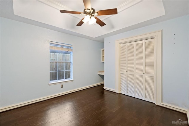 unfurnished bedroom featuring a tray ceiling, a closet, ceiling fan, and dark hardwood / wood-style flooring