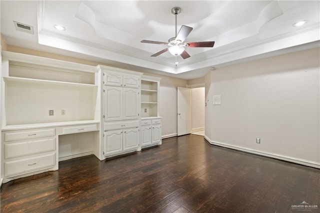 unfurnished office with dark hardwood / wood-style floors, ceiling fan, a raised ceiling, and built in desk