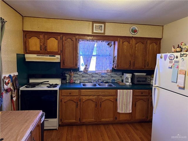 kitchen with under cabinet range hood, gas range oven, freestanding refrigerator, dark wood-style floors, and a sink