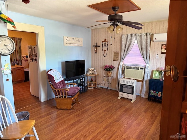 living room featuring heating unit, a ceiling fan, wood finished floors, cooling unit, and an AC wall unit