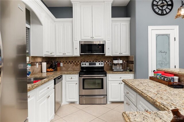 kitchen with white cabinets, stainless steel appliances, light stone counters, and tasteful backsplash